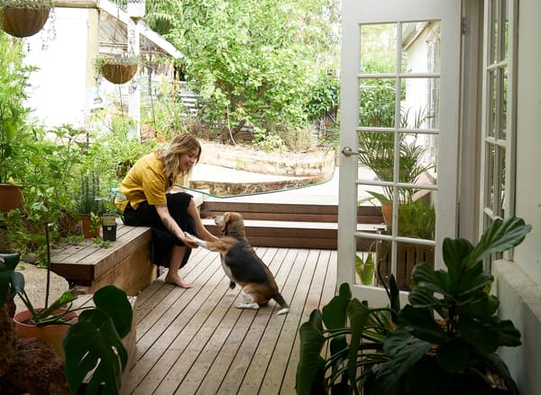 Nici et son chien assis sur une terrasse en bois dans un jardin devant une porte blanche.