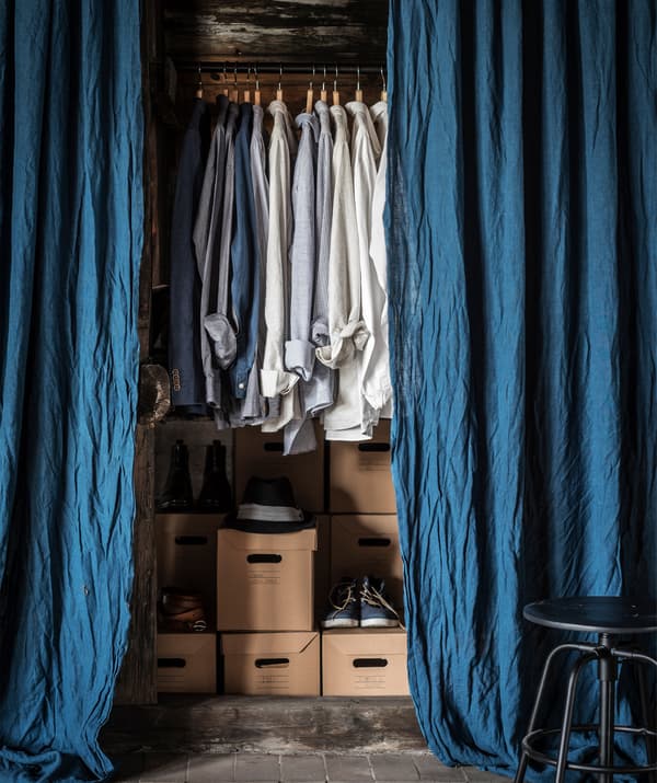Niebieskie zasłony zawieszone przy wieszaku z koszulkami i pudełkami z butami.