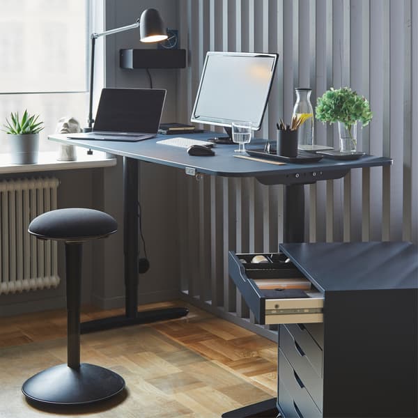 NILSERIK black/VISSLA black standing support in front of a sit-stand desk with computer screen in a home-office workspace. 
