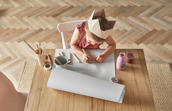 Niña con corona de reina pintando y dibujando en una mesa de madera con lápices de colores.