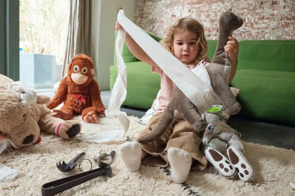 Niña jugando con papel blanco y peluches de mono, perro y conejo.