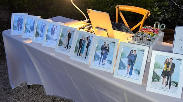Nine white FISKBO five by seven inch frames lined up on top of a table covered in a white tablecloth. Each frame holds a different live illustration of event guests and their attire.