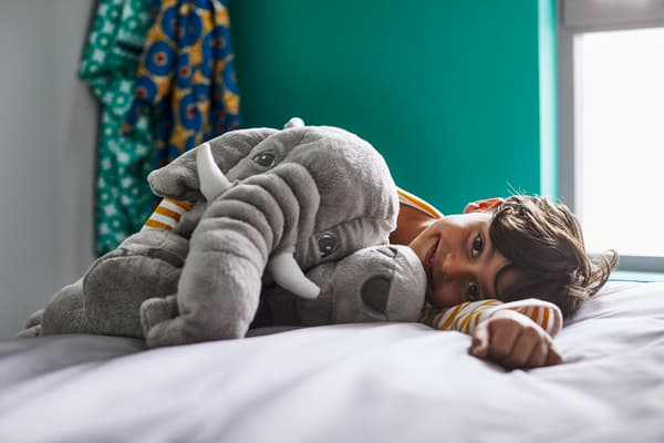 Niño acostado en la cama con peluche de elefante JÄTTESTOR.