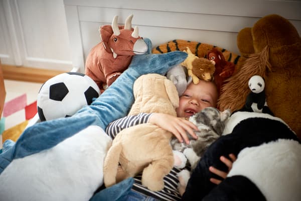 Niño acostado rodeado y tapado por peluches de juguetes