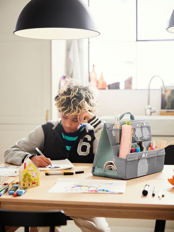 Niño estudiando en una mesa con organizador de escritorio, elementos de estudio y lámpara.