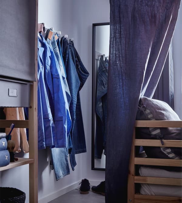 NISSEDAL mirror, with some jeans hanging on a hook rail in an open wardrobe nook by a bed.