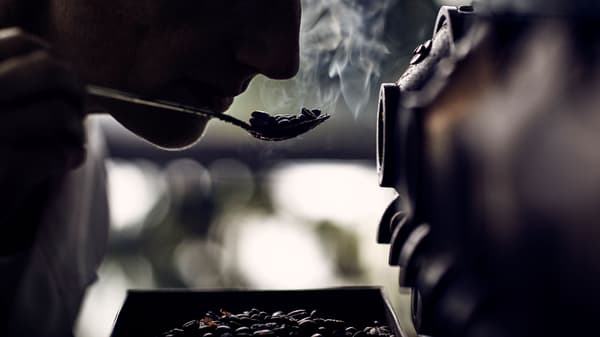 Nő vizsgálja a kávébabok illatát egy kanálon.