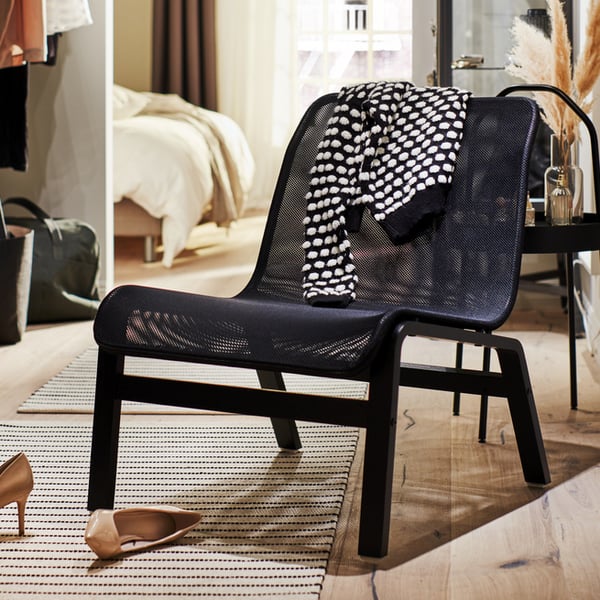 NOLMYRA easy chair in black on top of rug in hallway area, with a pair of high heels lying on the floor. 