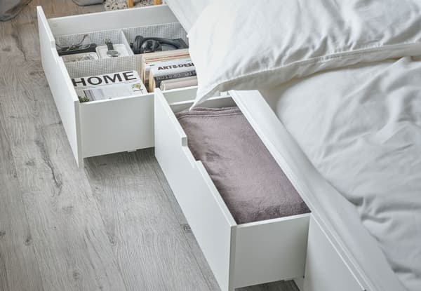 NORDLI bed with storage has drawers open, showing folded bed linen along with books, magazines, and accessories.