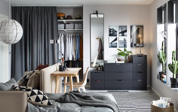 NORDLI kommode i antrasitt med ni skuffer mot en bakvegg i ei lita stue med en sovesofa og et skrivebord.