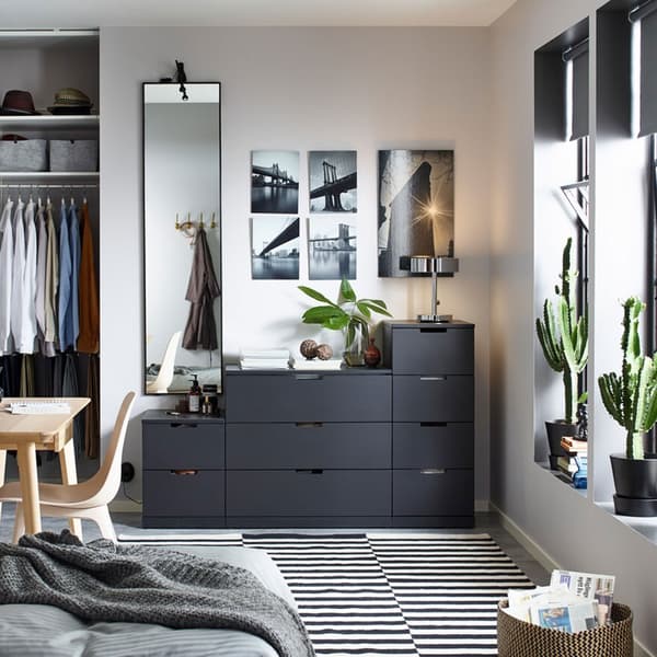 NORDLI Kommode mit 9 Schubladen in Anthrazit an einer Wand in einem kleinen Wohnraum mit Bettsofa und Schreibtisch