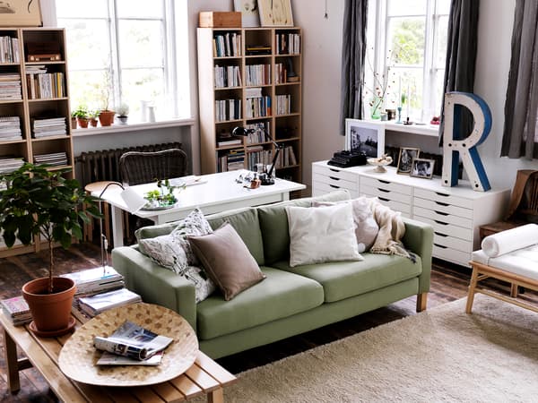 緑のソファと木製テーブルを置いたナチュラルなリビング。観葉植物と本棚で温かみのある空間。