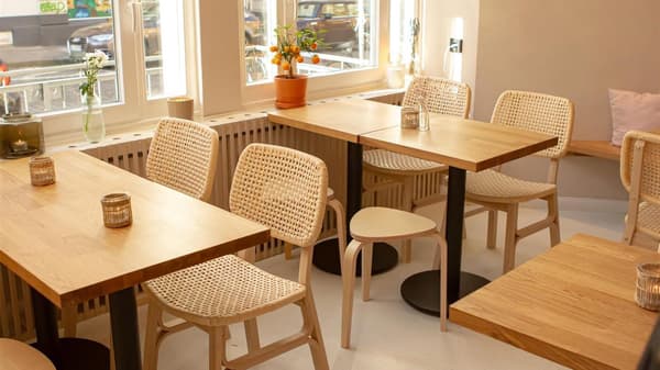 木のテーブルと籐の椅子が並ぶ、自然光が差し込む居心地のよいカフェの内装