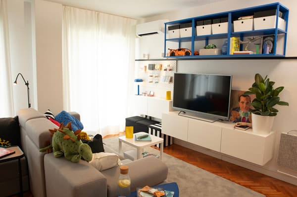 Nuevo salón con mueble para la televisión, estanterías, sofá, lámpara, mesa, accesorio y cortinas.