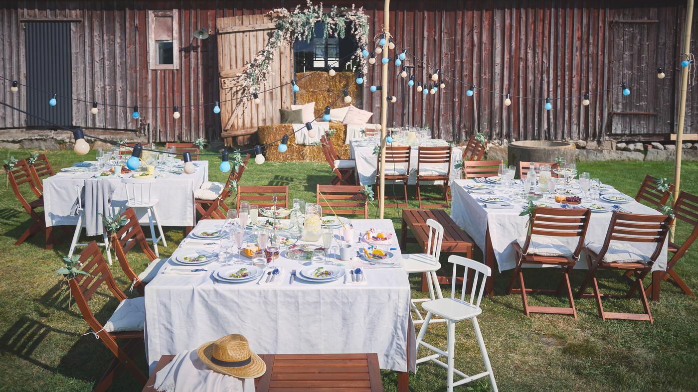Numa festa no exterior, as mesas estão decoradas com toalhas de mesa GULLMAJ, pratos UPPLAGA, copos DYRGRIP e talheres UPPHÖJD.