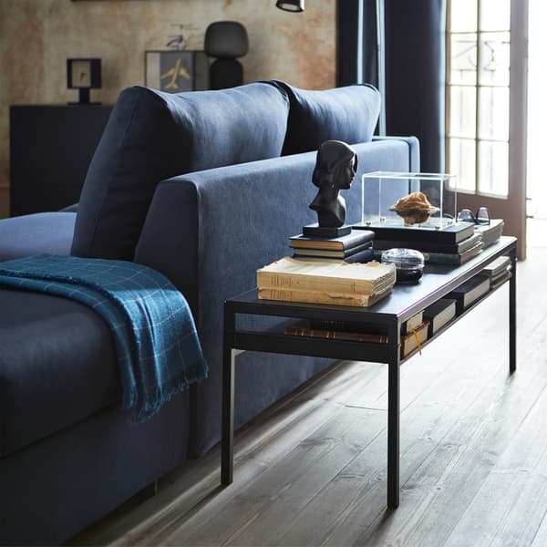 NYBODA coffee table with reversible table top in black/beige and it has some books, ornaments and a small bust placed on it.