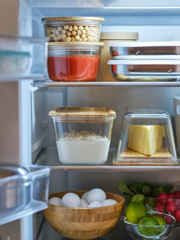 Nyitott ajtajú hűtőszekrény, belsejében IKEA 365+ ételtárolókban tárolt élelmiszerek és egy BLANDA MATT tál, amiben tojások láthatók.
