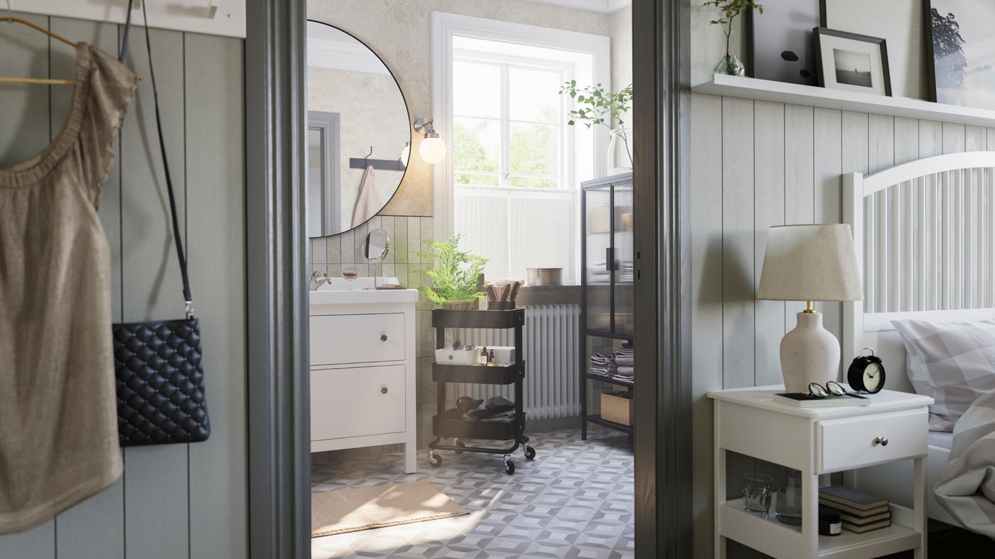 O baie gri cu o fereastră mare, în care se află o mască de lavoar HEMNES albă, un cărucior RÅSKOG negru și un corp cu ușă de sticlă MOSSJÖN.