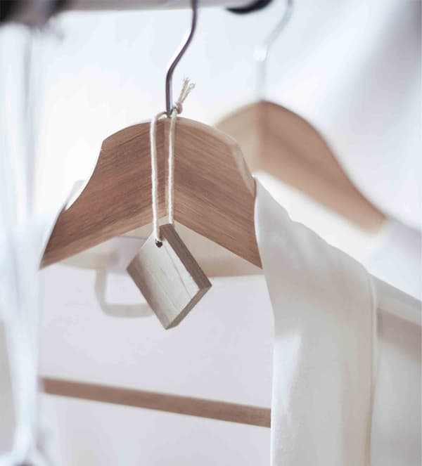 O bucată din lemn de cedru agățată de umerașul pe care este pusă o cămașă albă din material tare.
