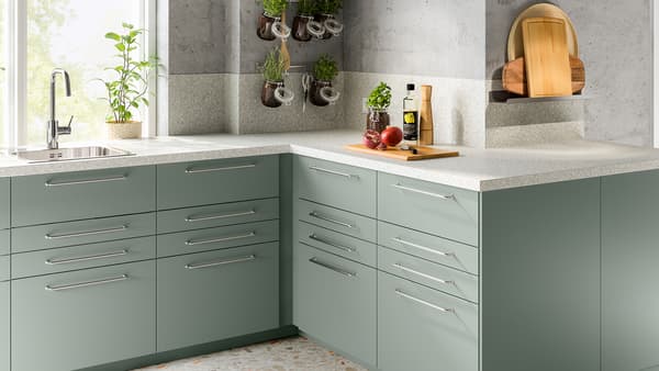 O bucătărie de colț cu un blat gri deschis cu efect mineral și câteva dulapuri cu fronturi de sertare cu folie gri-verde.