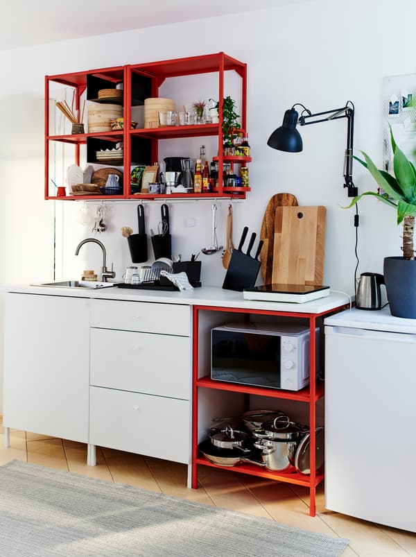 O bucătărie mică, bine echipată, formată dintr-o combinație de unități ENHET – unități de depozitare deschisă roșii și închisă albe.
