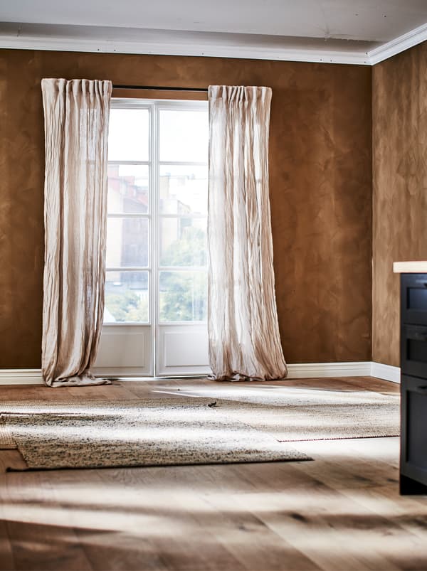 O cameră maro cu ferestre în stil franțuzesc, cu perdele din in creponat și un covor LOHALS maro deschis pe pardoseala din lemn.