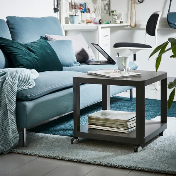 O canapea verde și o măsuță de cafea gri cu rotile, așezate pe un covor bicolor, cu albastru și verde deschis.