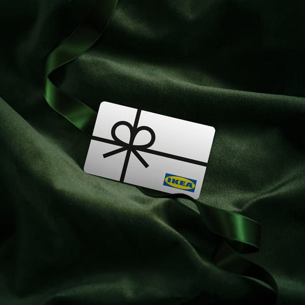 O card cadou IKEA alb, cu un desen de fundă neagră, așezat pe un material verde închis, cu o panglică verde.