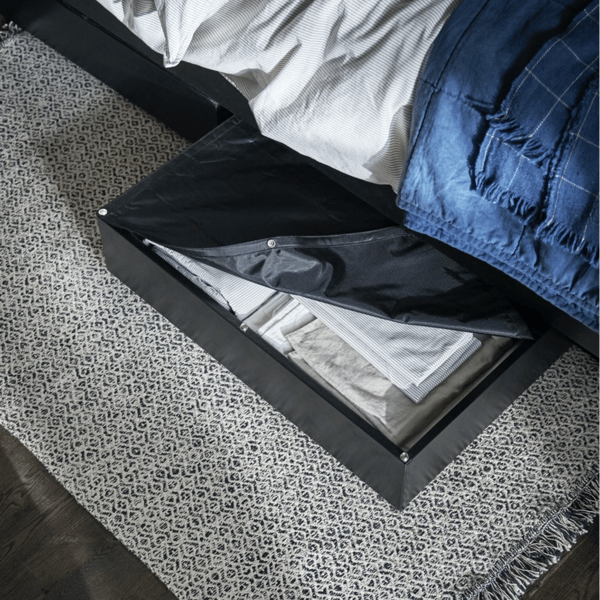 O cutie de depozitare LYCKSELE ușor deschisă, care se întrezărește de sub pat. În cutia de depozitare se află o lenjerie de pat împăturită.