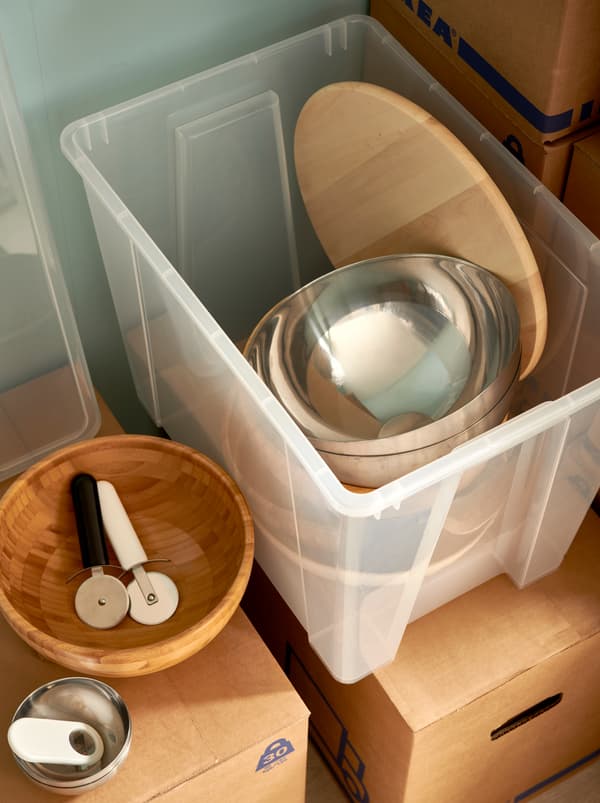 O cutie de plastic SAMLA plină cu boluri de servire BLANDA, un platou rotativ și veselă, toate așezate pe cutii JÄTTENE una peste alta.