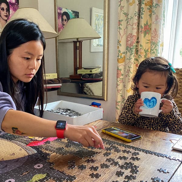 O femeie construiește un puzzle pe o măsuță de cafea. Fiica ei stă lângă ea, bând dintr-o cană.