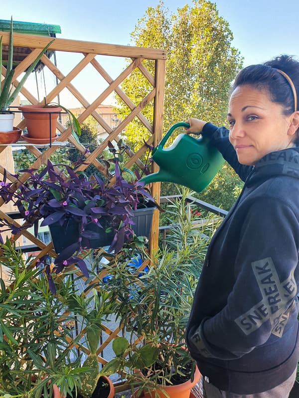 O femeie îmbrăcată cu un hanorac negru udă plantele cu o stropitoare verde.