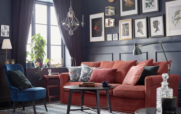 O încăpere cu lambriuri închise la culoare, în stil tradițional, cu lucrări de artă înrămate, o canapea GRÖNLID roșie cu perne și o măsuță de cafea KRAGSTA.