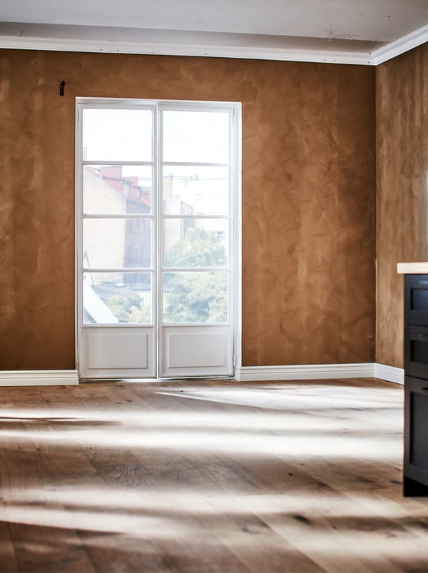 O încăpere goală cu ferestre în stil franțuzesc, pardoseală din lemn și perete zugrăvit într-un ton de maroniu bogat, cu finisaj mat catifelat.
