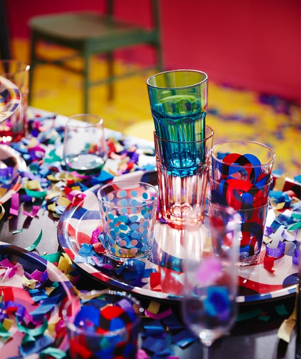 O masă de petrecere cu confetti și o tavă cu pahare FRAMKALLA  și POKAL cu roșu și albastru.