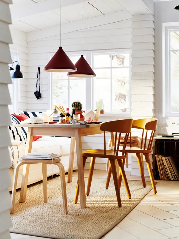 O masă NORRÅKER înconjurată de scaune OMTÄNKSAM formează o un set de masă într-o încăpere albă, învăluită de razele soarelui, cu lambriu pe pereți.