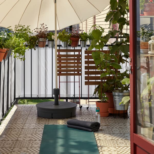 O masă și un scaun pliate și așezate într-o parte, pentru a face spațiu unui covor de yoga întins pe podeaua balconului. 