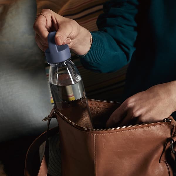 O sticlă de plastic refolosibilă IKEA 365+ care este scoasă dintr-o geantă din piele maro.