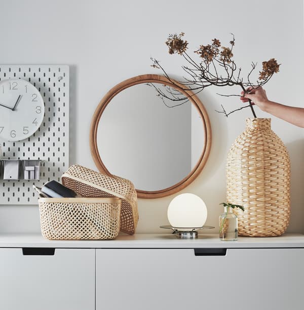 O vază decorativă KAFFEBÖNA și o cutie SMARRA din bambus pe partea de sus a unui corp alb.