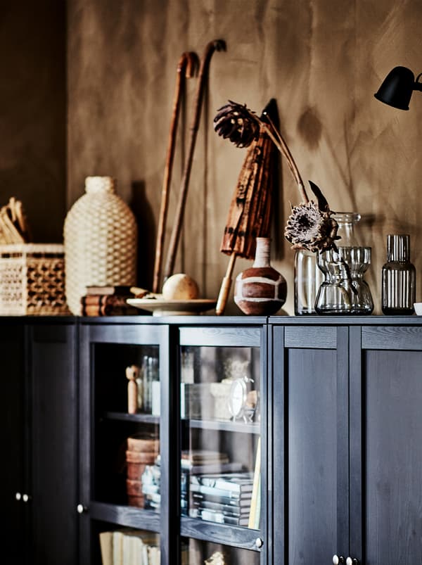 Obiecte personale aduse din călătorii, obiecte din materiale naturale și vaze din sticlă cu flori pe partea de sus a unui corp HAVSTA maro închis.