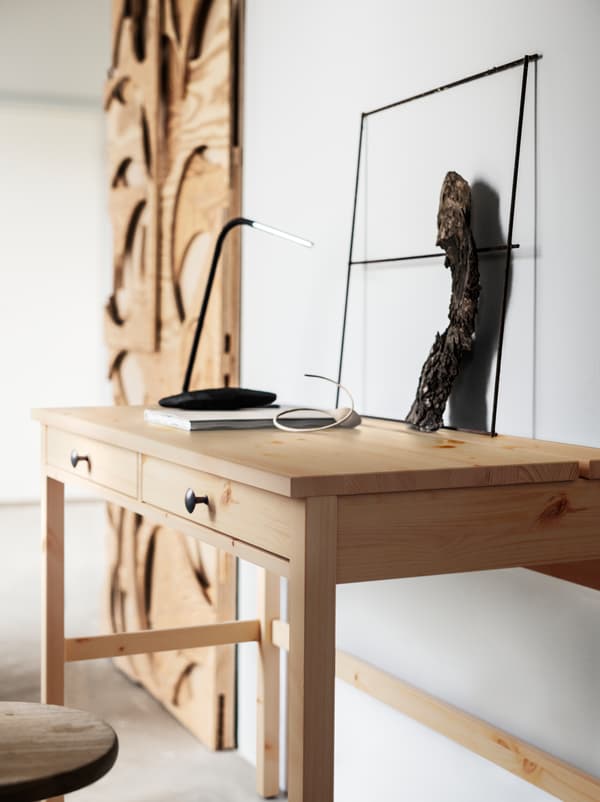 Objetos feitos de madeira clara não tratada, colocados ao longo de uma parede numa divisão em branco. Um deles é uma elegante secretária HEMNES com gavetas.