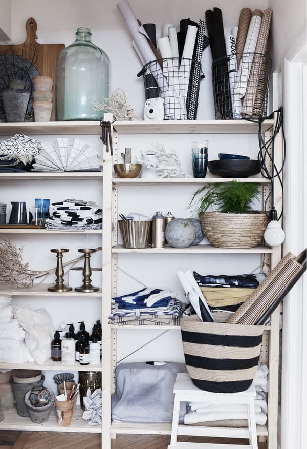 Objets en verre, textiles et plantes sur des étagères ouvertes.