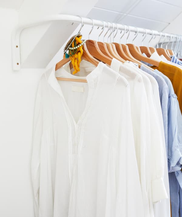 Oblečenie zavesené na drevených vešiakoch na bielej tyči v bielej miestnosti.