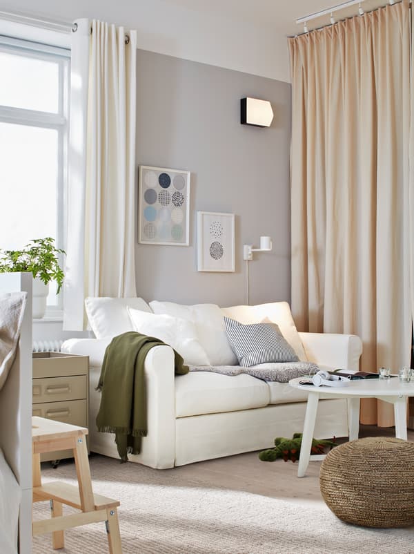 Obývacia izba s bielou pohovkou GRÖNLID, konferenčným stolíkom a sedadlom. Na vzdialenej stene sú závesy dlhé až po zem.