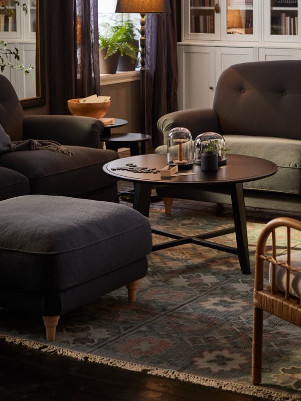 Obývacia izba s dvomi tmavosivými pohovkami ESSEBODA, na zemi je koberec VESTERVIG, na ňom stoja tri čierne okrúhle stolíky KRAGSTA a podnožka ESSEBODA.