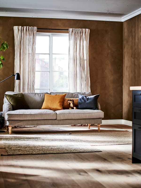 Obývacia izba s francúzskymi oknami, pokrčenými ľanovými závesmi, pohovkou s vankúšmi, lampou SKURUP a kobercami z prírodných materiálov.