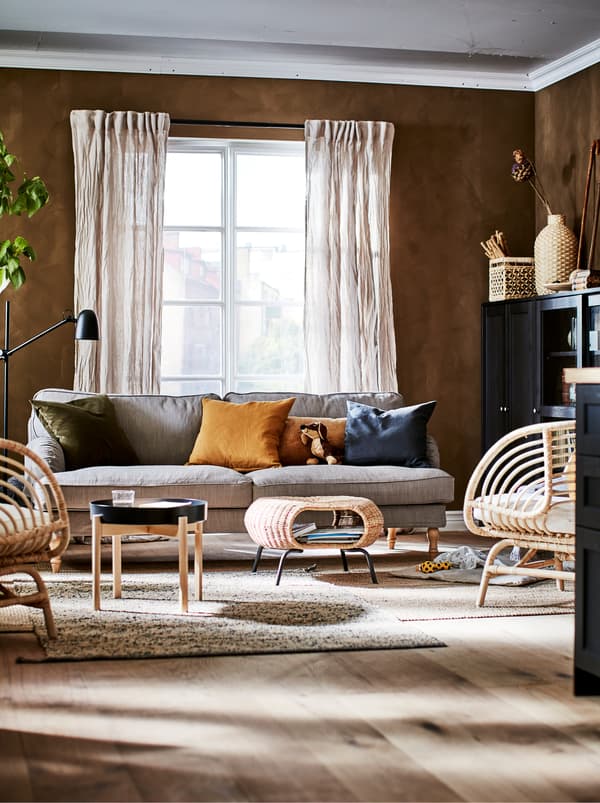 Obývacia izba v zemitých farbách s dekoráciami, úložnými priestormi, kreslami BUSKBO, pohovkou, príručnými stolíkmi a rastlinou. 