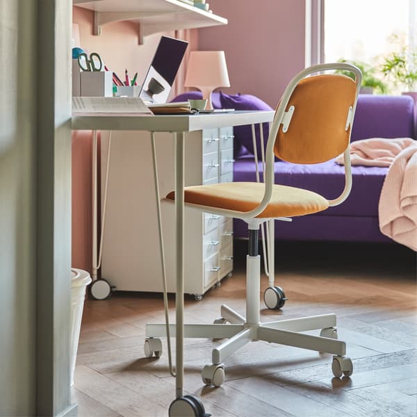 ÖRFJÄLL white swivel chair with VISSLE dark yellow cover in a small home office with a table, filling cabinets and bed sofa.