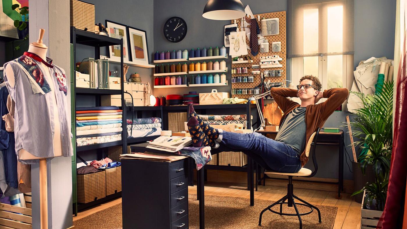 Oficina en casa para taller de costura, chico sentado en una silla inclinado hacia atrás con los pies sobre el escritorio.