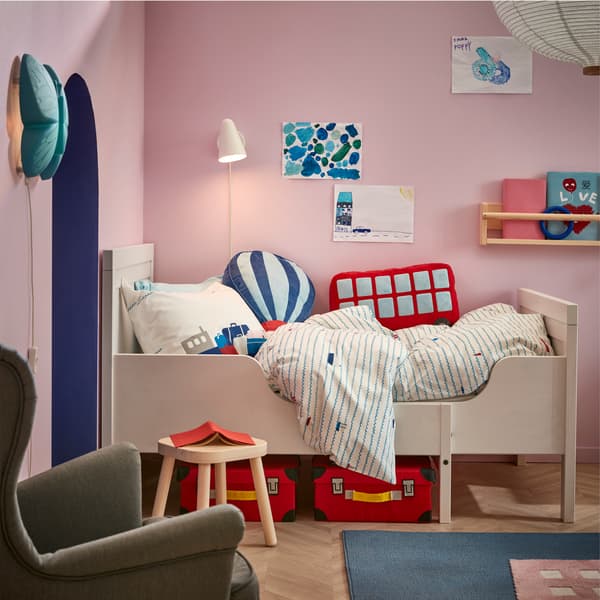 Okvir belog produživog dečjeg kreveta s tekstilima sa šarom brodića i upaljena bela zidna lampa iznad.